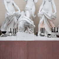 White marble statues with subtle textures, set against a warm, rust-colored backdrop and sleek black candle holders.