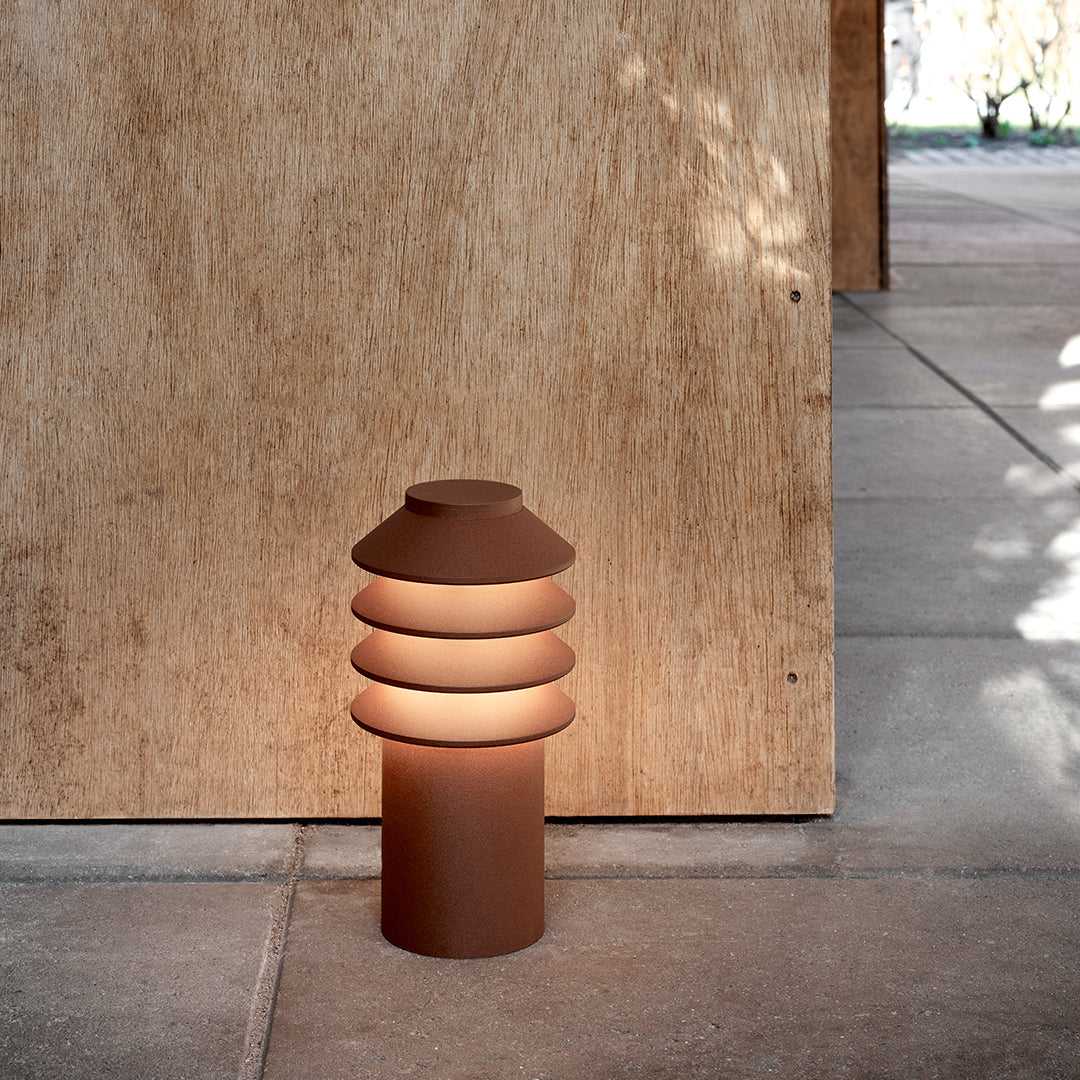 Brown stacked lamp with a smooth, rounded design, casting warm light against a textured beige wall.