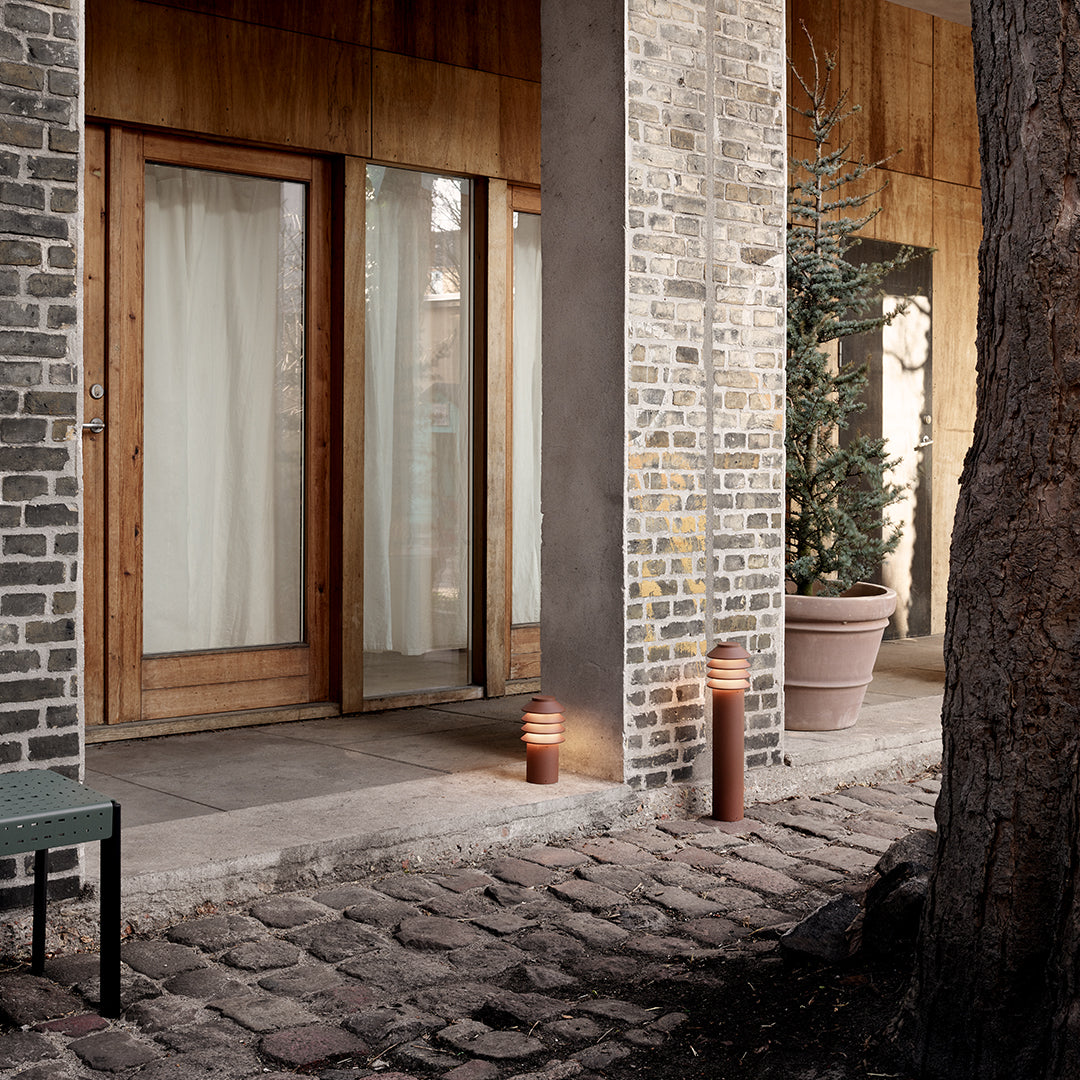 "Neutral-toned outdoor setting featuring textured stone and warm wood tones, accented by soft white drapes and greenery."