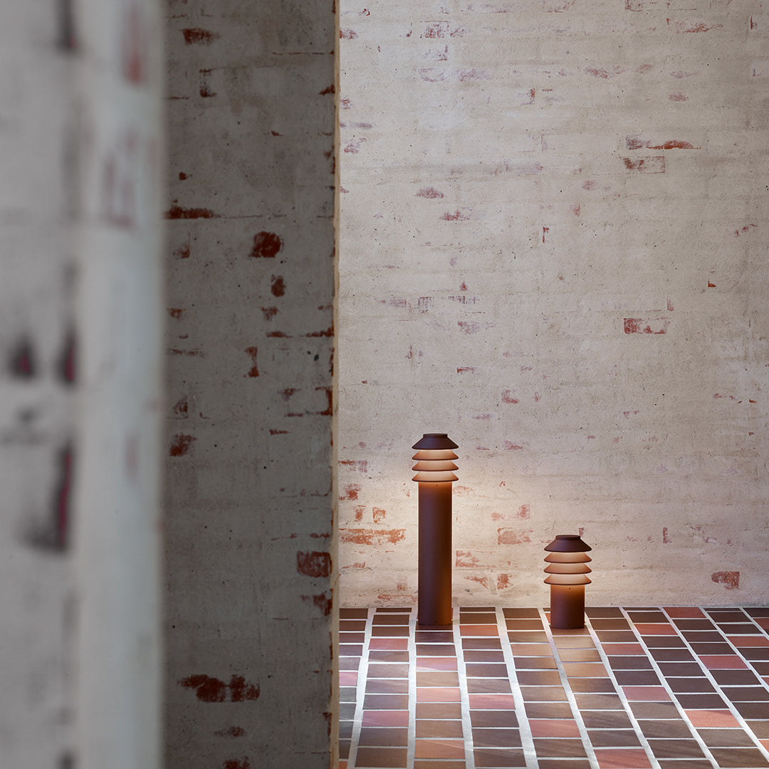 Brown and white striped lamps on a textured, multi-colored tile floor against a rustic brick wall backdrop.