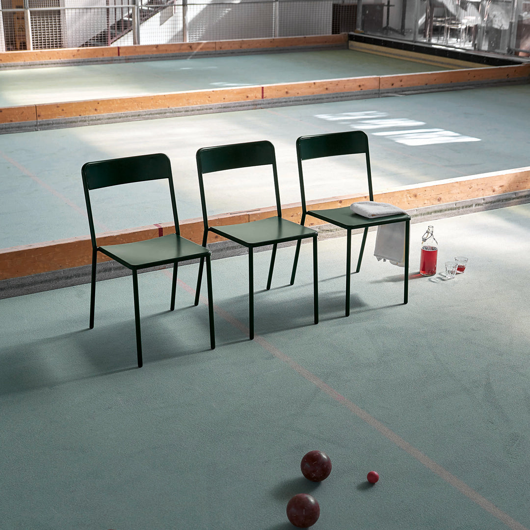 Three green metal chairs on a light green floor, creating a minimalist and modern seating arrangement.