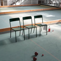 Three green metal chairs on a light green floor, creating a minimalist and modern seating arrangement.