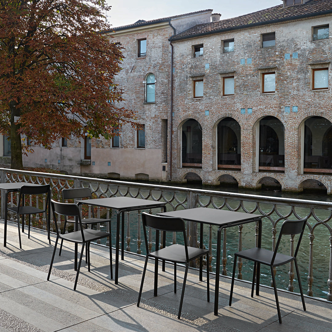 Modern black outdoor furniture set with sleek lines, set against a rustic stone backdrop and calm water reflections.
