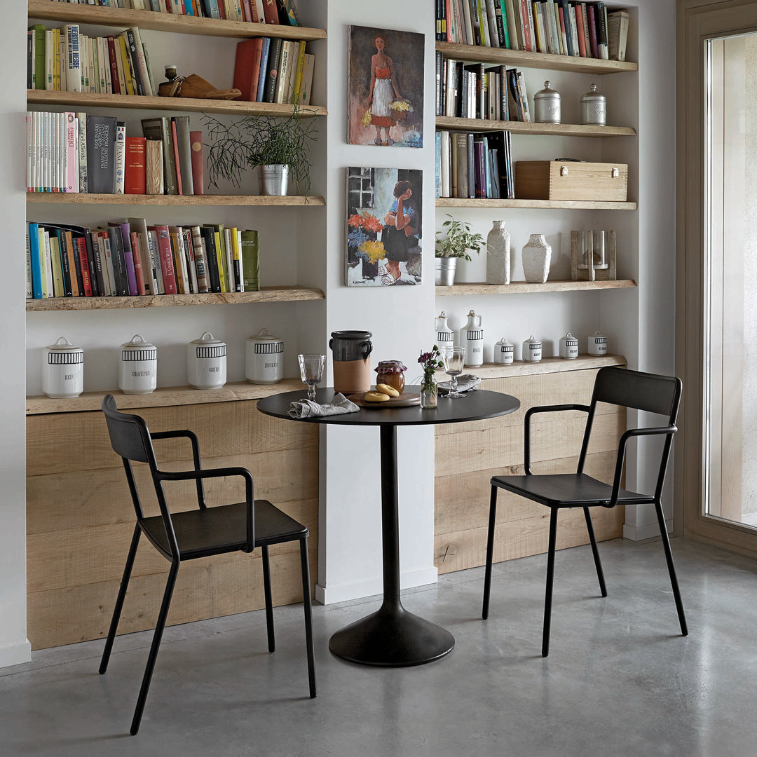 Black dining table with patterned chairs in a bright interior with wooden shelves and books.