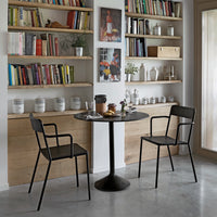 Black dining table with patterned chairs in a bright interior with wooden shelves and books.