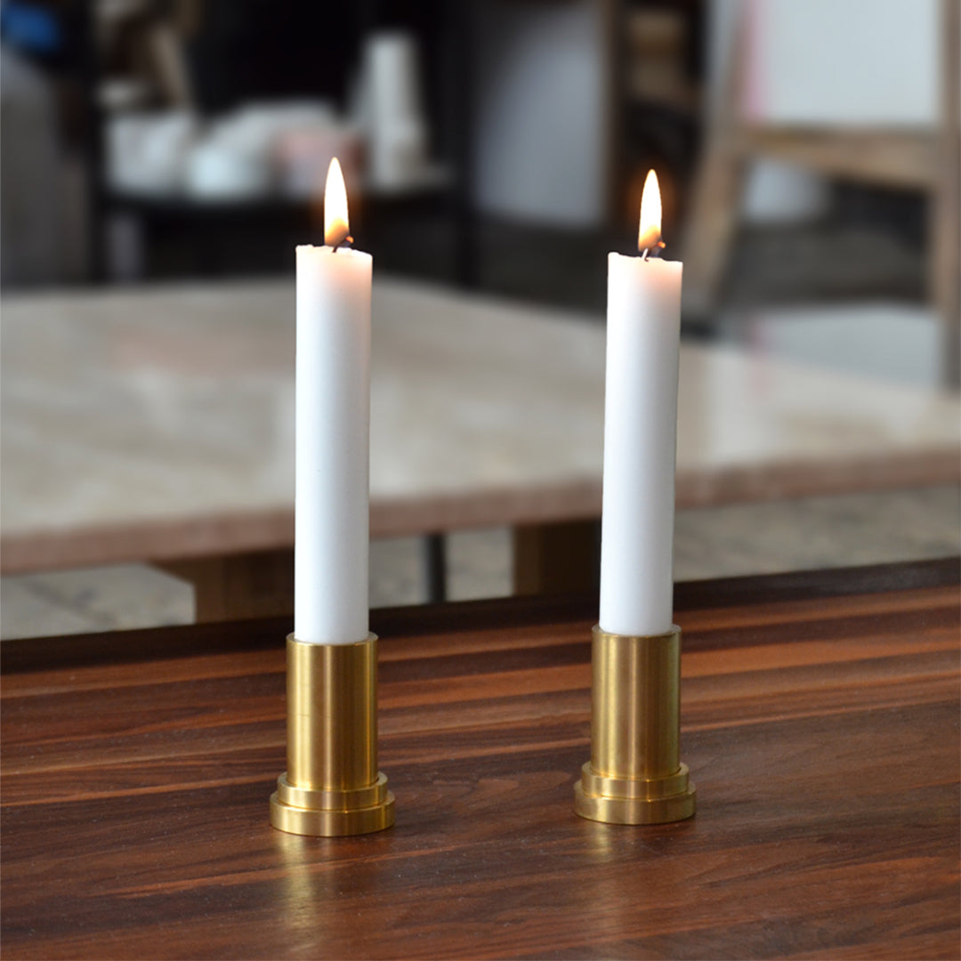 White candles in gold holders, flickering flames on a wooden table. Elegant and modern design adds a warm touch.