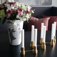 Elegant white candle holders with gold accents and a patterned vase featuring floral designs. Dark background enhances colors.