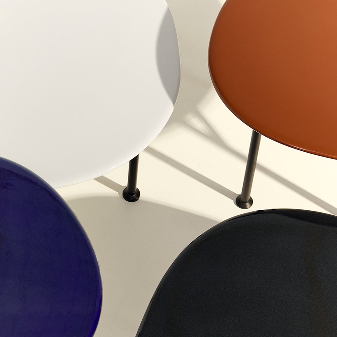 Colorful round tabletops in white, brown, deep blue, and black with sleek black legs. Modern design and vibrant patterns.