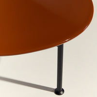 Round, glossy orange tabletop with sleek black metal legs against a neutral background. Modern design, minimalistic style.