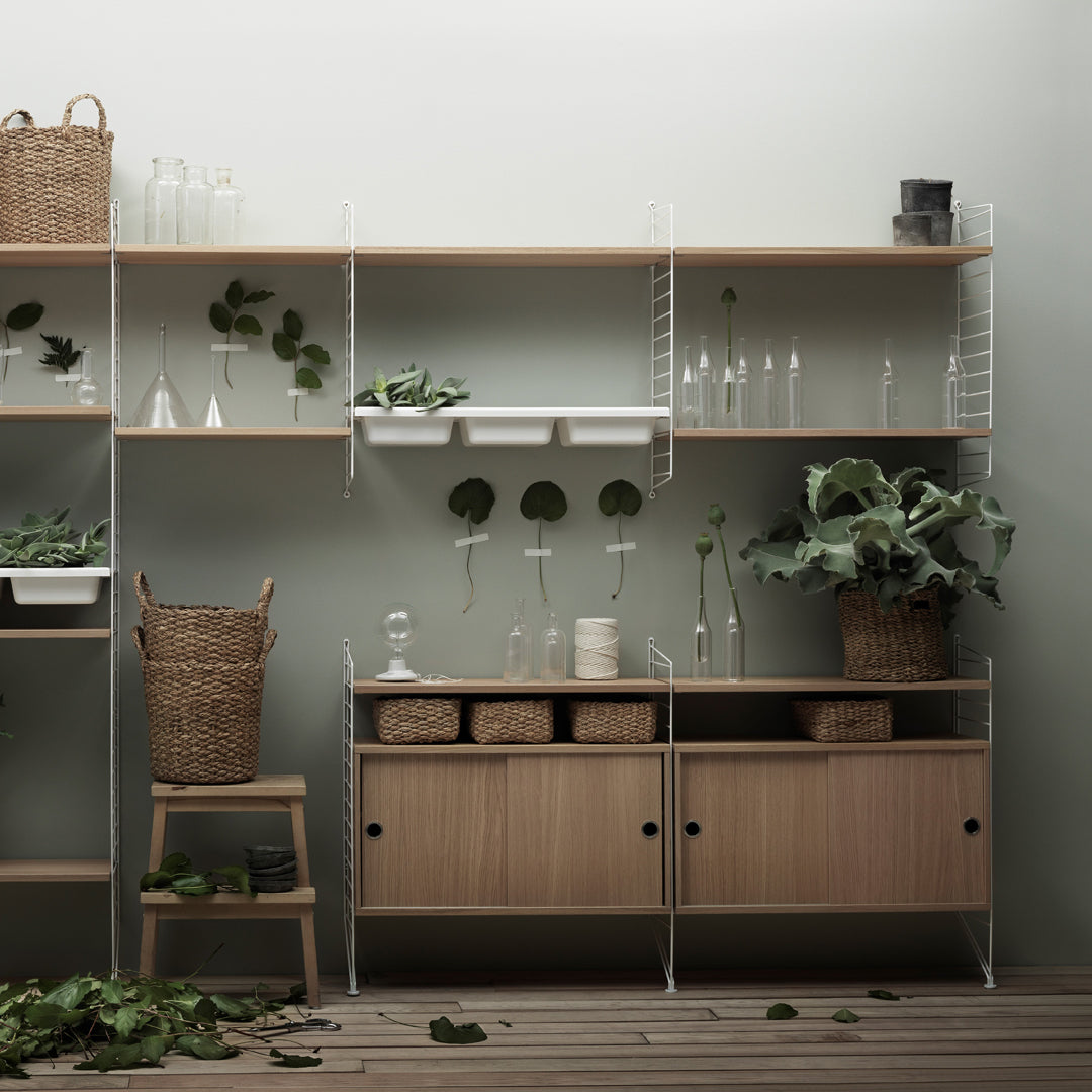Light wood shelves and cabinets with clear glass accents, featuring green plants and natural woven textures.