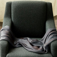 Soft gray satin draped over a textured green chair, showcasing a subtle gradient of tones. Ideal for cozy decor.