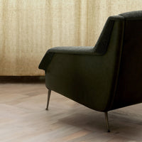 Dark green armchair with a textured dark gray cushion, set against a warm, light wood floor and soft beige curtains.