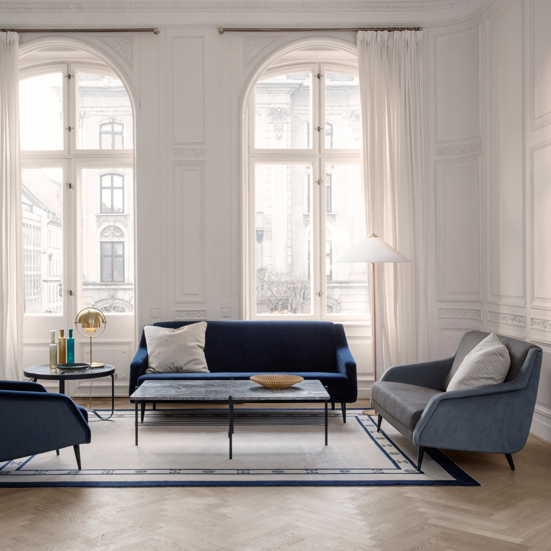 Navy blue and light gray sofas with a geometric patterned rug in a bright, airy room with white walls and large windows.