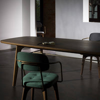 Modern wooden dining table with a rich dark finish, complemented by green upholstered chairs against a minimalist backdrop.
