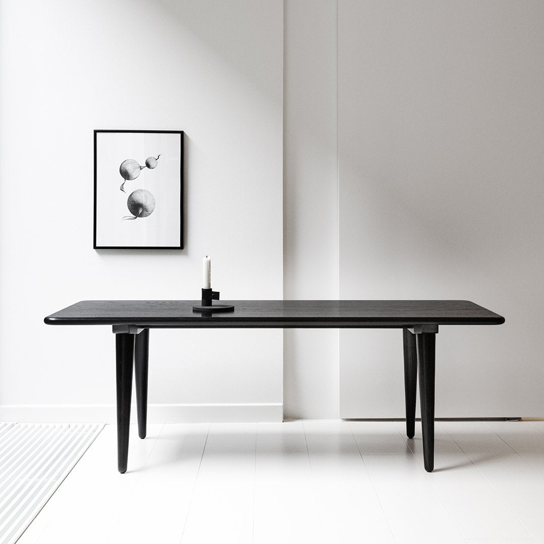 Sleek black dining table with minimalist design, smooth surfaces, and tapered legs, set against a neutral backdrop.