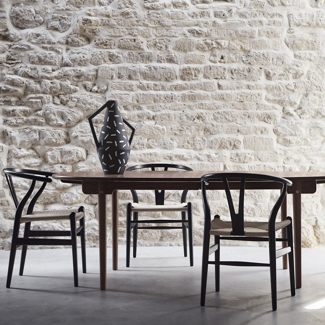Black and natural woven chairs around a wooden table, with a decorative black vase featuring a geometric pattern.
