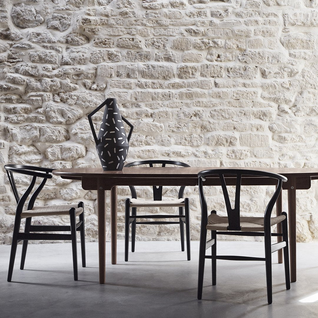 Black and natural wood dining chairs with a patterned black vase against a textured stone wall backdrop.