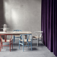 Colorful chairs in red, blue, and white around a wooden table, with a deep purple curtain in a modern interior setting.