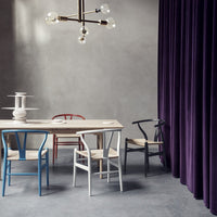 Colorful dining chairs in blue, red, white, and black around a light wood table, set against a rich purple curtain.