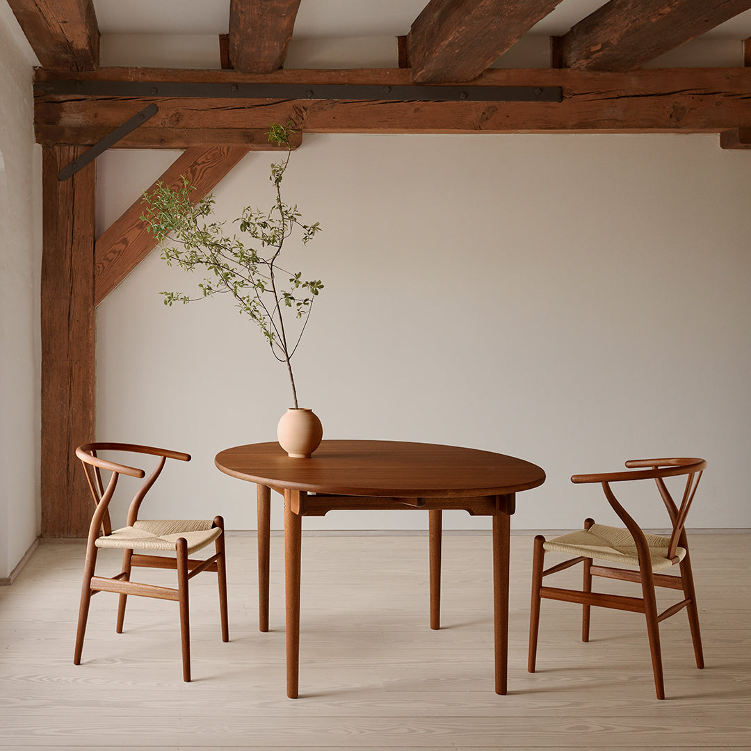 Rustic wooden table with a smooth, oval surface; classic wooden chairs featuring woven seats in a neutral tone.