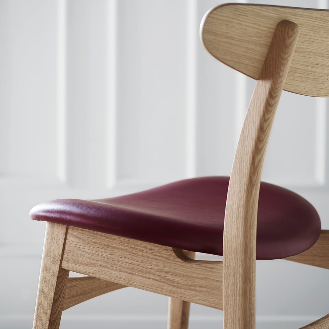 Elegant wooden chair with a rich burgundy seat and smooth, natural oak finish. Ideal for modern decor.