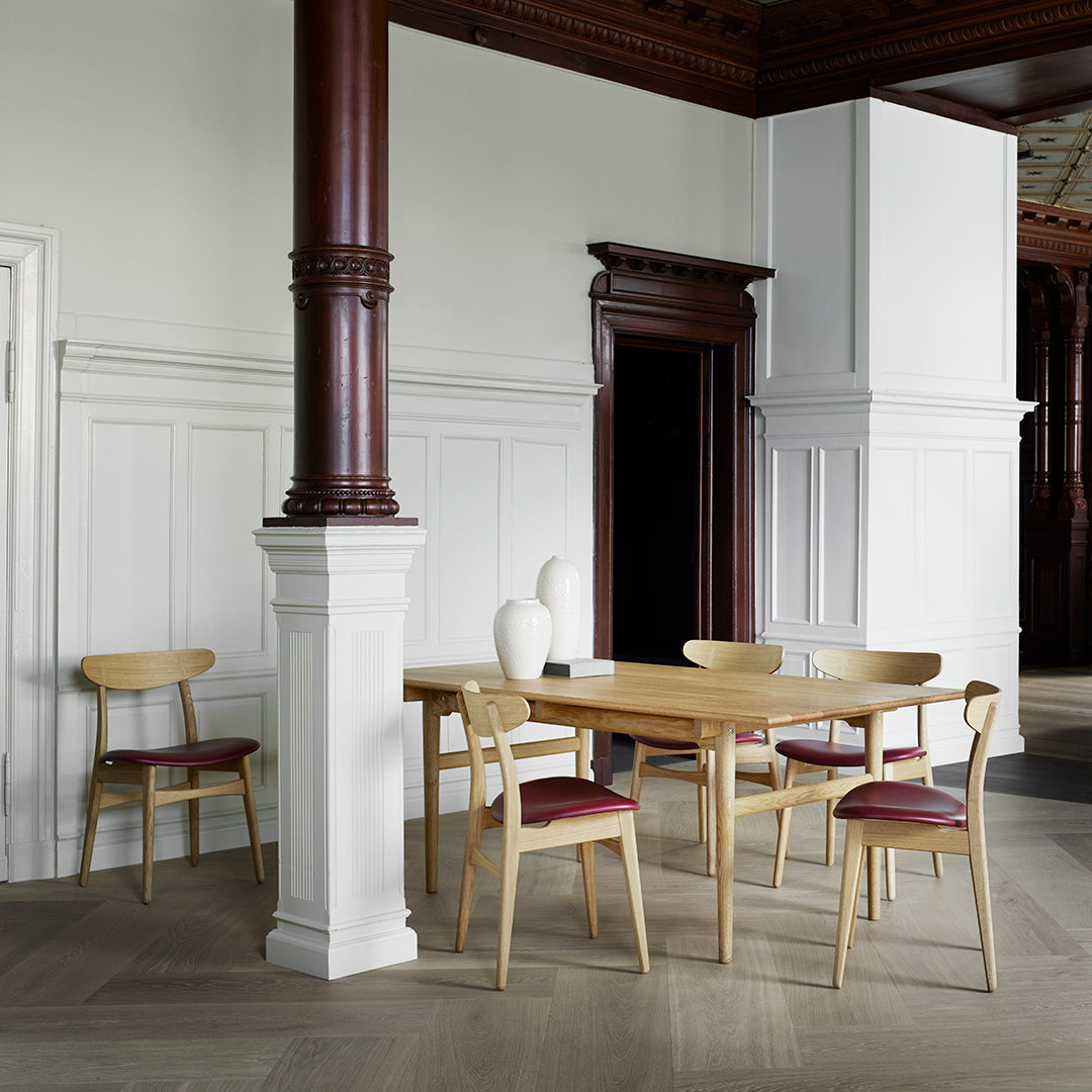 Light wood dining table set with beige and burgundy accents, featuring sleek lines amidst a minimalist interior.