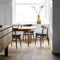 Minimalist dining room with a wooden table and chairs, featuring earthy tones and clean lines. Elegant amber vase adds warmth.