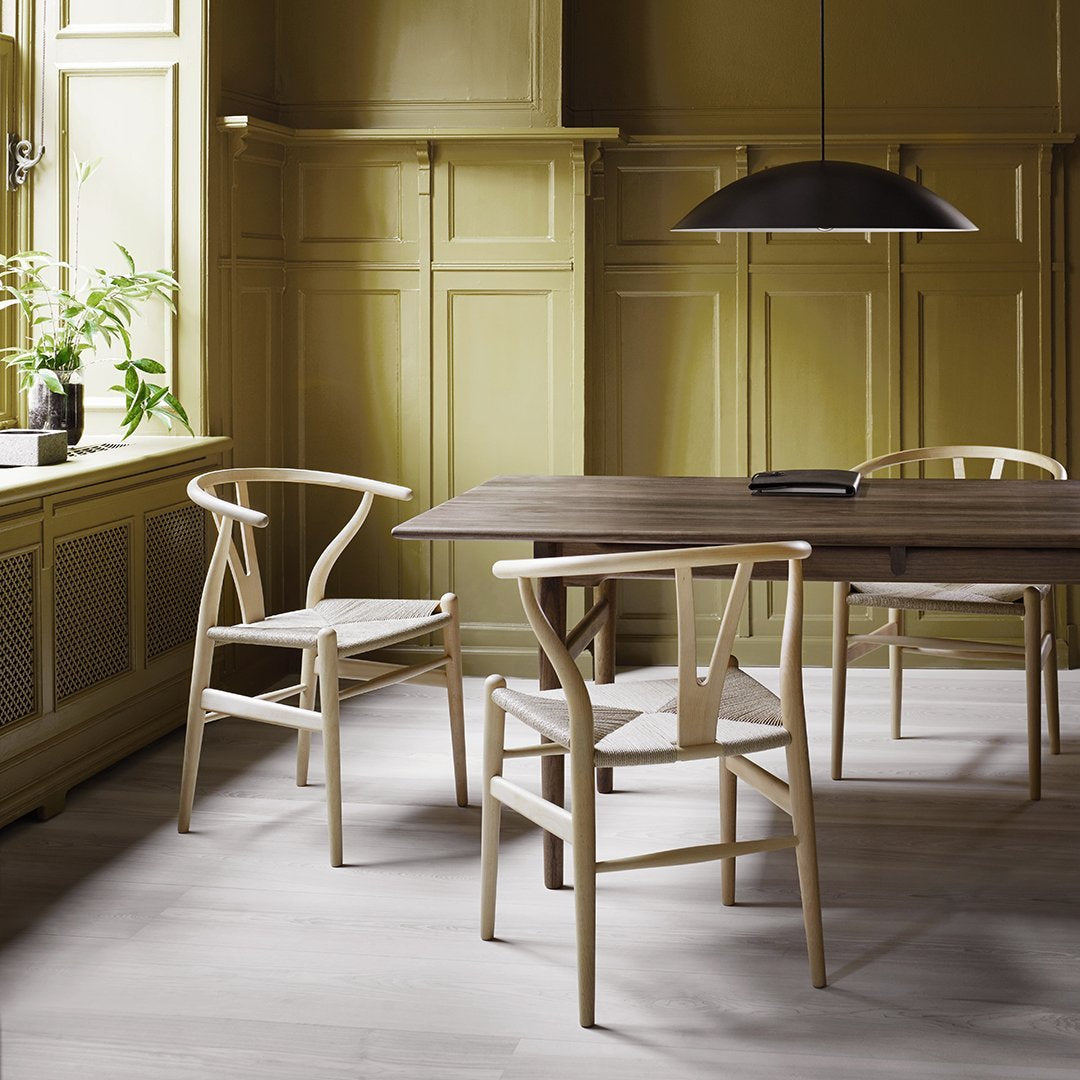 Light wooden chairs and dark table against warm olive green walls, complemented by a sleek black pendant light.