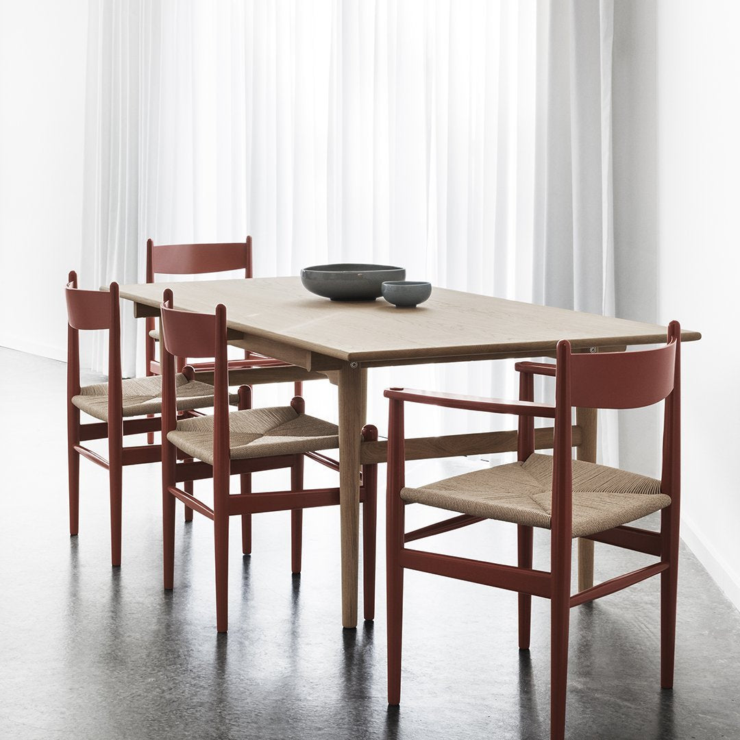 Light wood dining table with rust-red chairs featuring a minimalist design and beige seat cushions.