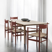 Light wood dining table with rust-red chairs featuring a minimalist design and beige seat cushions.