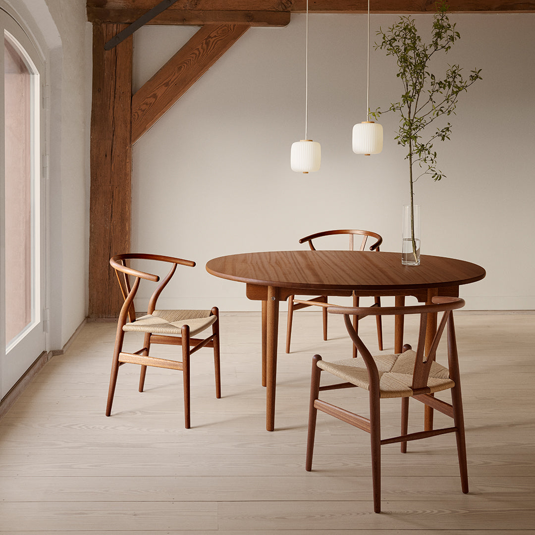 "Wooden round dining table with a warm brown finish and two minimalist pendant lights against a neutral backdrop."