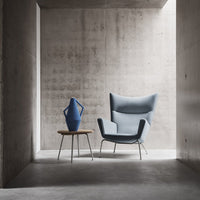 Light blue chair and blue vase on a wooden table against a minimalist concrete backdrop. Modern design elements.