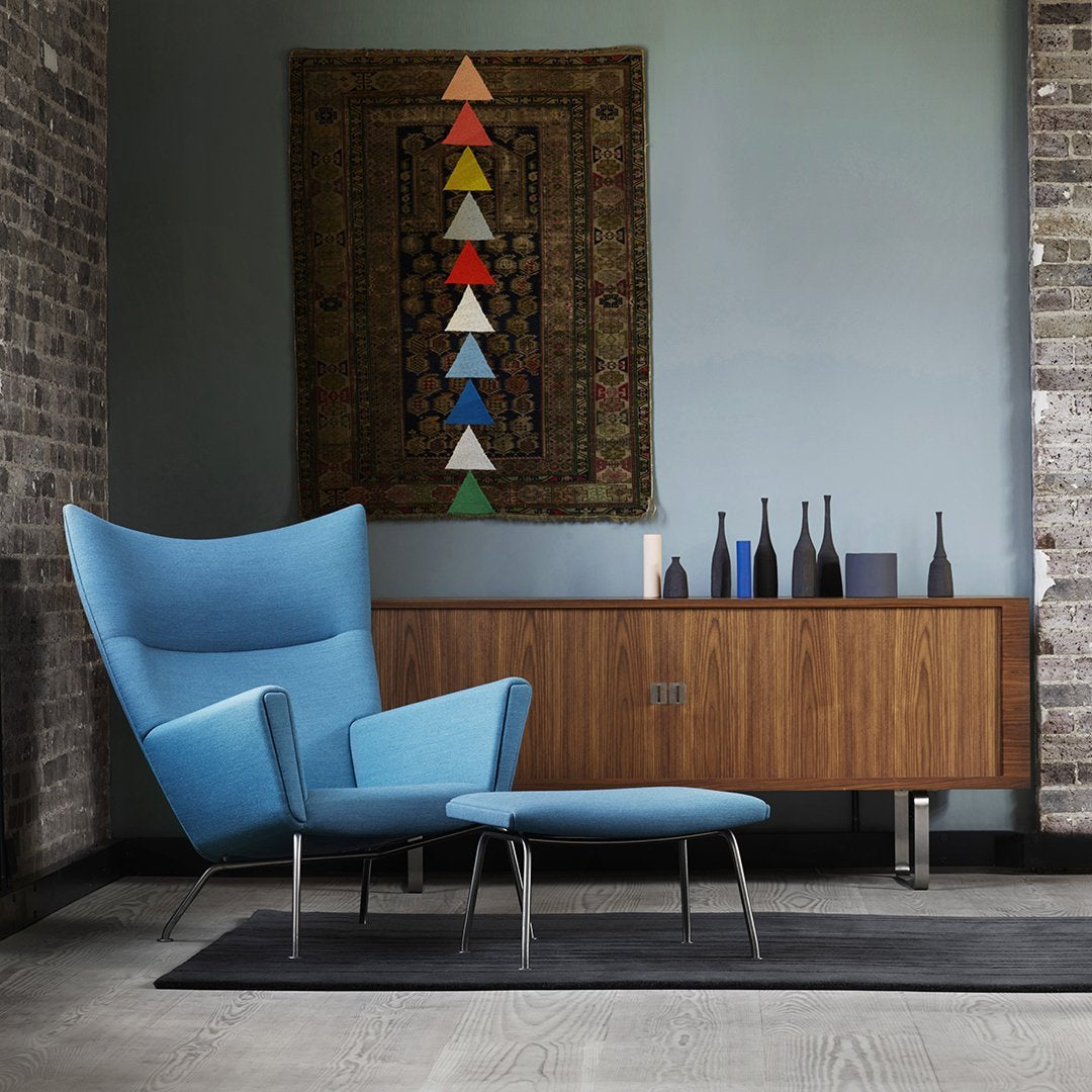 Light blue armchair and ottoman paired with a wooden cabinet, featuring colorful triangular art and dark blue decor accents.