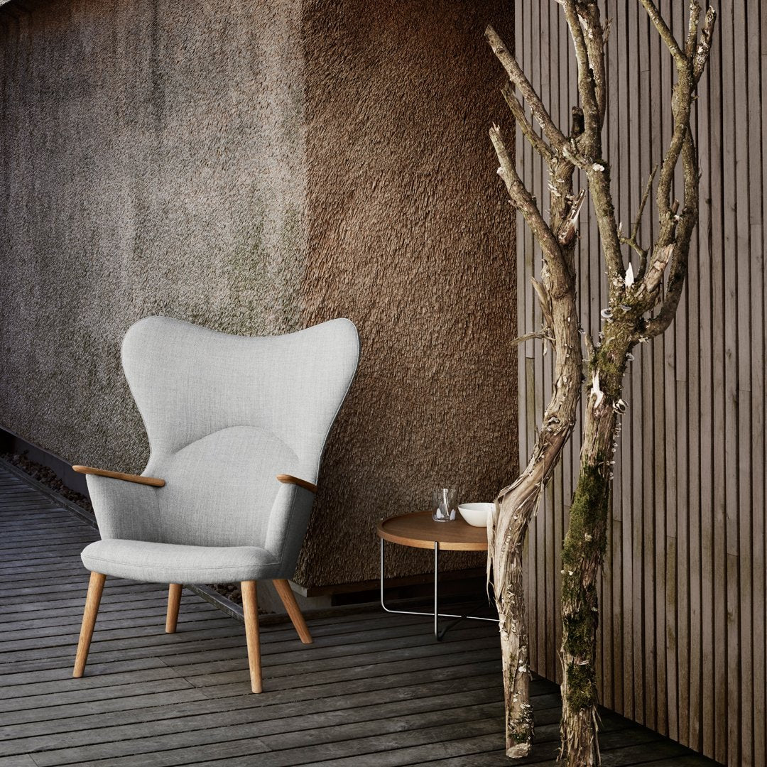 Light gray upholstered chair with a contemporary, winged design, paired with natural wood accents against a textured wall.