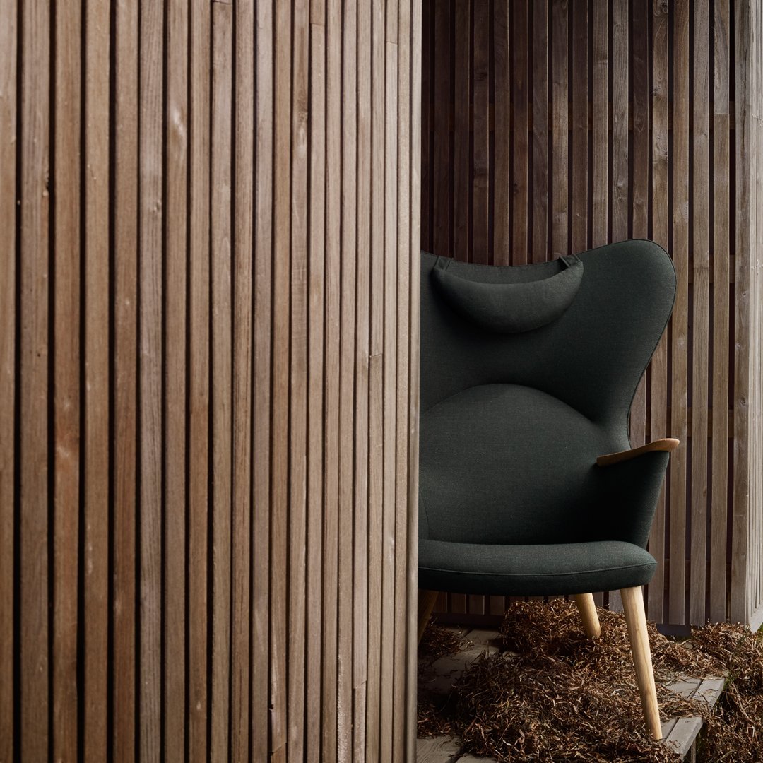 Stylish dark green upholstered armchair with a smooth surface and wooden legs, set against textured wooden panels.