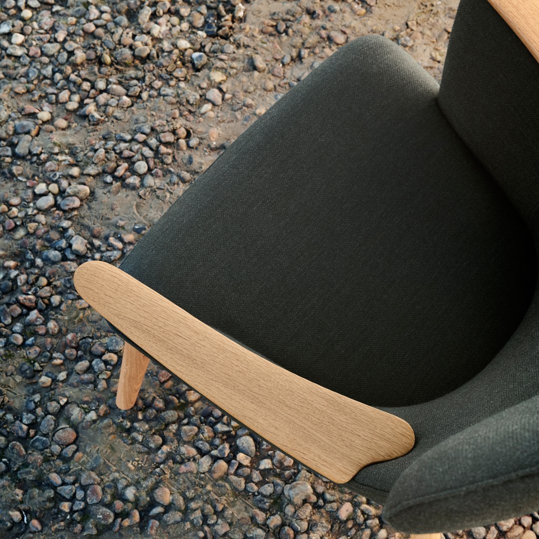 Gray upholstered chair with a smooth wooden armrest, set against a textured gravel background.