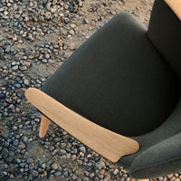 Gray upholstered chair with a smooth wooden armrest, set against a textured gravel background.