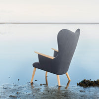 Gray upholstered chair with a curved back and natural wood legs, set against a serene water background.