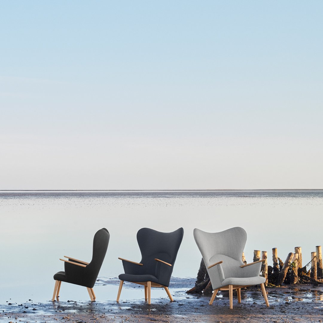 Three stylish chairs: black, dark gray, and light gray, with smooth fabric and wooden armrests, set against a tranquil backdrop.
