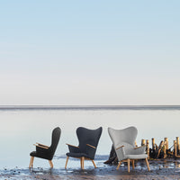 Three stylish chairs: black, dark gray, and light gray, with smooth fabric and wooden armrests, set against a tranquil backdrop.