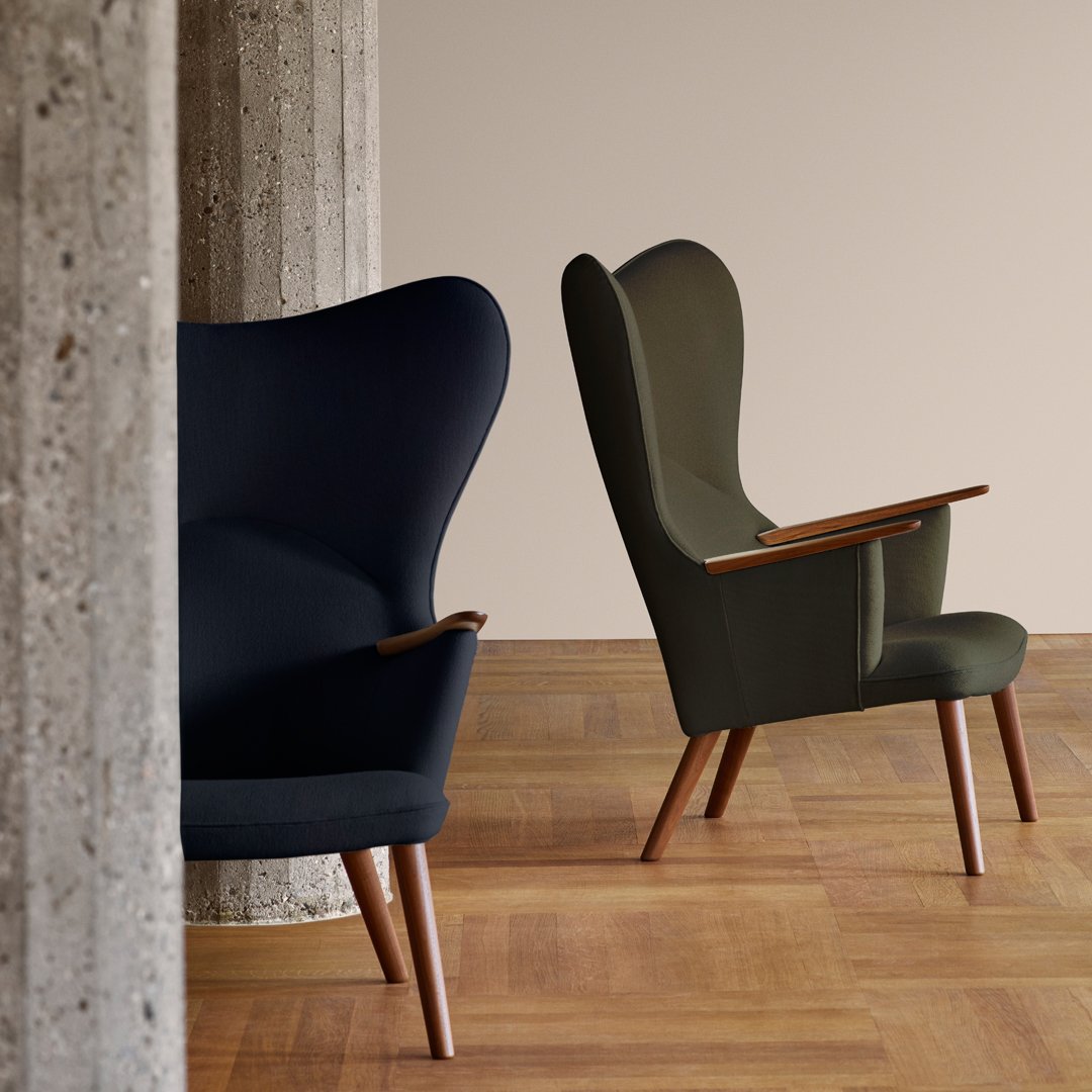 "Two stylish chairs in deep navy and olive green fabrics with wood accents, set against a neutral backdrop."