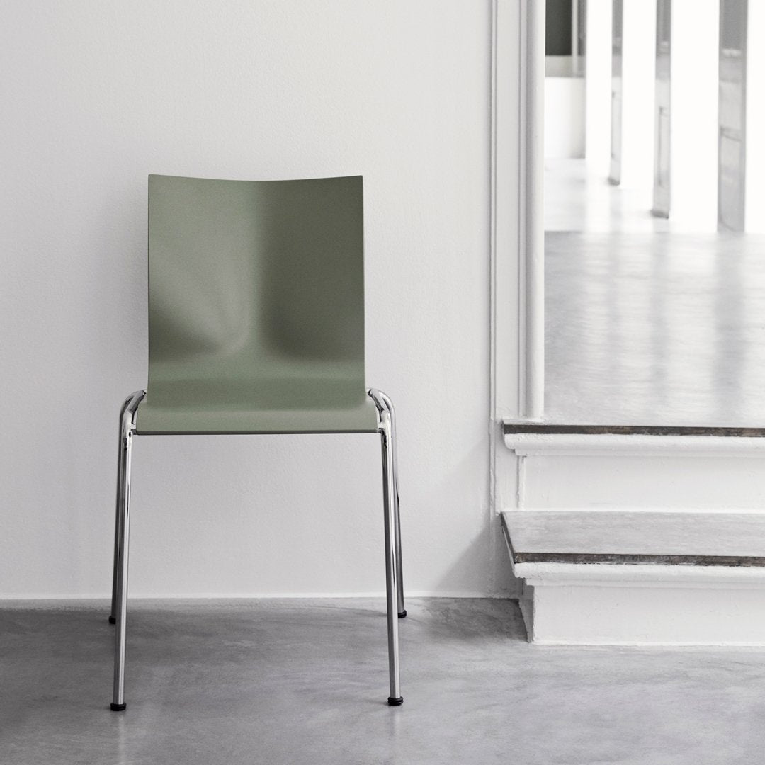 Modern green chair with a smooth, matte finish and sleek chrome legs, set on a minimalist concrete floor.