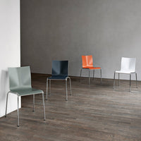 Colorful modern chairs in green, navy, orange, and white with sleek designs on a wooden floor against a gray wall.