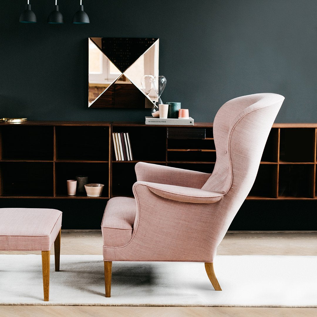 Light pink velvet armchair with gold legs, complemented by a matching ottoman against a dark wall.