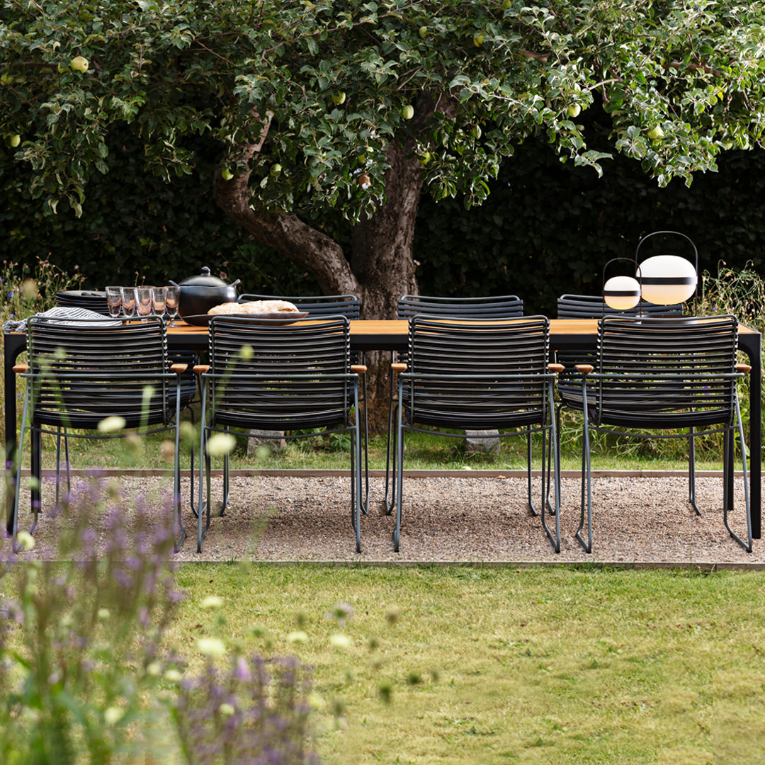 Modern black striped outdoor dining chairs arranged around a wooden table in a lush green garden setting.