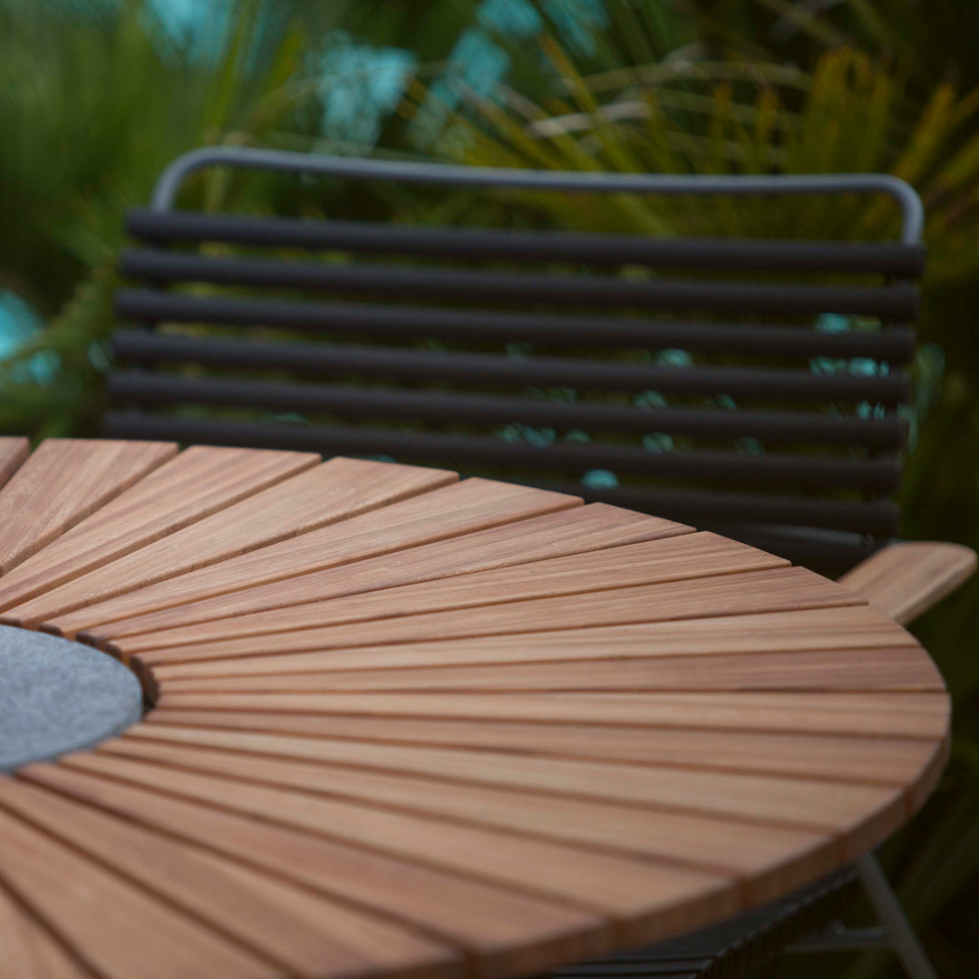 Round wooden table with a sunburst pattern and a gray center, complemented by a sleek black striped chair.