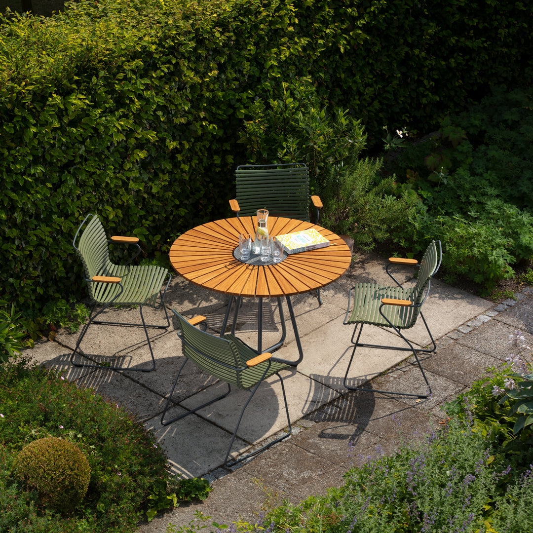 "Round wooden table with green striped chairs in a lush garden setting."