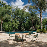 Green chairs and a round wooden table, set against a lush, tropical backdrop with bright blue skies and palm trees.