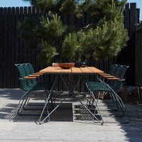 "Outdoor dining set featuring a wooden tabletop and green wire chairs against a natural backdrop."