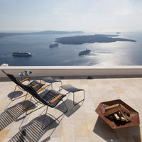 "Black and wooden lounge chairs with a sleek design, against a backdrop of blue ocean and sunny skies."